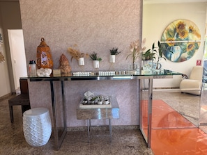 A reception desk with a glass top, surrounded by decorative items and plants. - Rosa Spa e Pousada (Aparecida de Goiânia)
