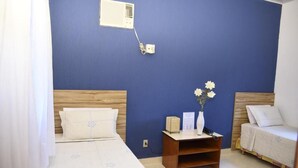A bedroom with a blue wall, a wooden headboard, a white bed with a floral pattern, a bedside table with a vase and a lamp, and a small wooden nightstand.