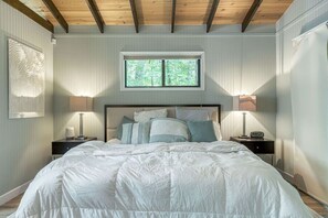 A bedroom with a large bed, two bedside tables, a window, and a wooden ceiling. - Romantic Escape at Innsbrook by Sarah Bernard (Innsbrook)