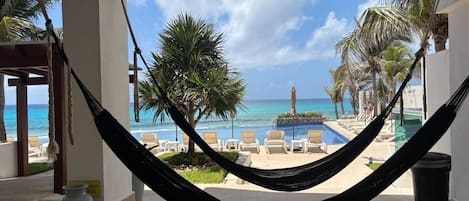 A hammock in a room with a view of a pool and palm trees.