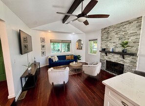 A spacious living area with a dark wood floor, a blue sofa, a white armchair, a round coffee table, and a fireplace with a stone wall. - 3 Bedroom Chatsworth Lake Manor Oasis (chatsworth)