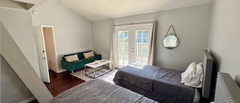 A room with two beds, a ceiling fan, a window with curtains, and a small table.