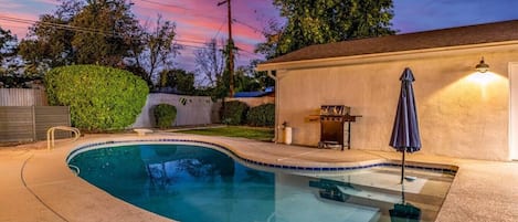 Una piscina con hidromasaje, una parrilla de barbacoa y un patio cubierto.