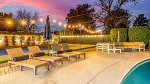 Un espace aménagé au bord de la piscine, avec des chaises longues, une table et des guirlandes lumineuses.
