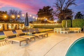 A poolside area with lounge chairs, a table, and string lights. - Pickleball Ball Paradise (Phoenix)