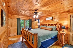 A wooden cabin bedroom with a bed, a ceiling fan, and a view of the outdoors. - Moonshine Romance Wood Cabin Retreat (Sevierville)