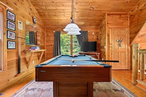 A wooden interior with a pool table, a television, and framed pictures on the wall. - Moonshine Romance Wood Cabin Retreat (Sevierville)