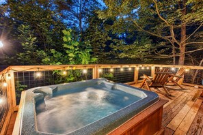 Ein Whirlpool auf einer Holzterrasse, umgeben von Bäumen, mit Lichterketten.