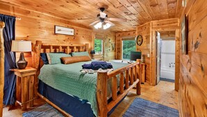 Camera da letto in una baita di legno, con un letto, comodini, una ventola a soffitto e vista sull'esterno.