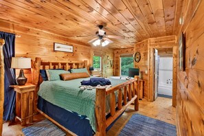 Ein Schlafzimmer einer Holzhütte mit Bett, Nachttischen, Deckenventilator und Blick ins Freie.