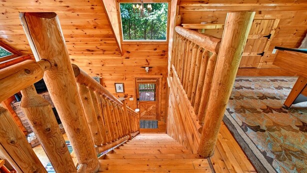 Un interno in legno con una scala che conduce a un livello inferiore, una finestra con vista sugli alberi e una porta con un pannello di vetro.