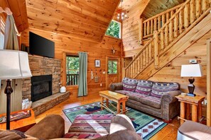 Ein Holzblockhaus-Interieur mit Kamin aus Stein, einer Couch, einem Couchtisch und einer Treppe.
