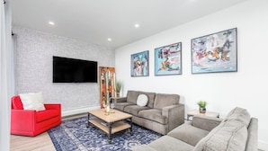 Una sala de estar moderna con pared de ladrillo, un televisor de pantalla plana y tres cuadros abstractos.