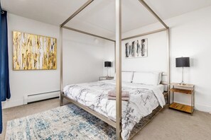 A four-poster bed with a marble-patterned bedspread, two bedside tables with lamps, and artwork on the walls.