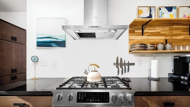 Cocina moderna con estufa de acero inoxidable, armarios de madera y estante empotrado con utensilios de cocina.