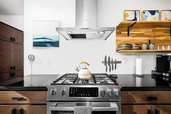 A modern kitchen with a stainless steel stove, wooden cabinets, and a wall-mounted shelf with kitchenware.