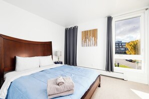 A hotel room with a large bed, a nightstand, a window with curtains, and a view of the outside. - Design-forward Anchorage Townhome w/ Ocean Views (Anchorage)