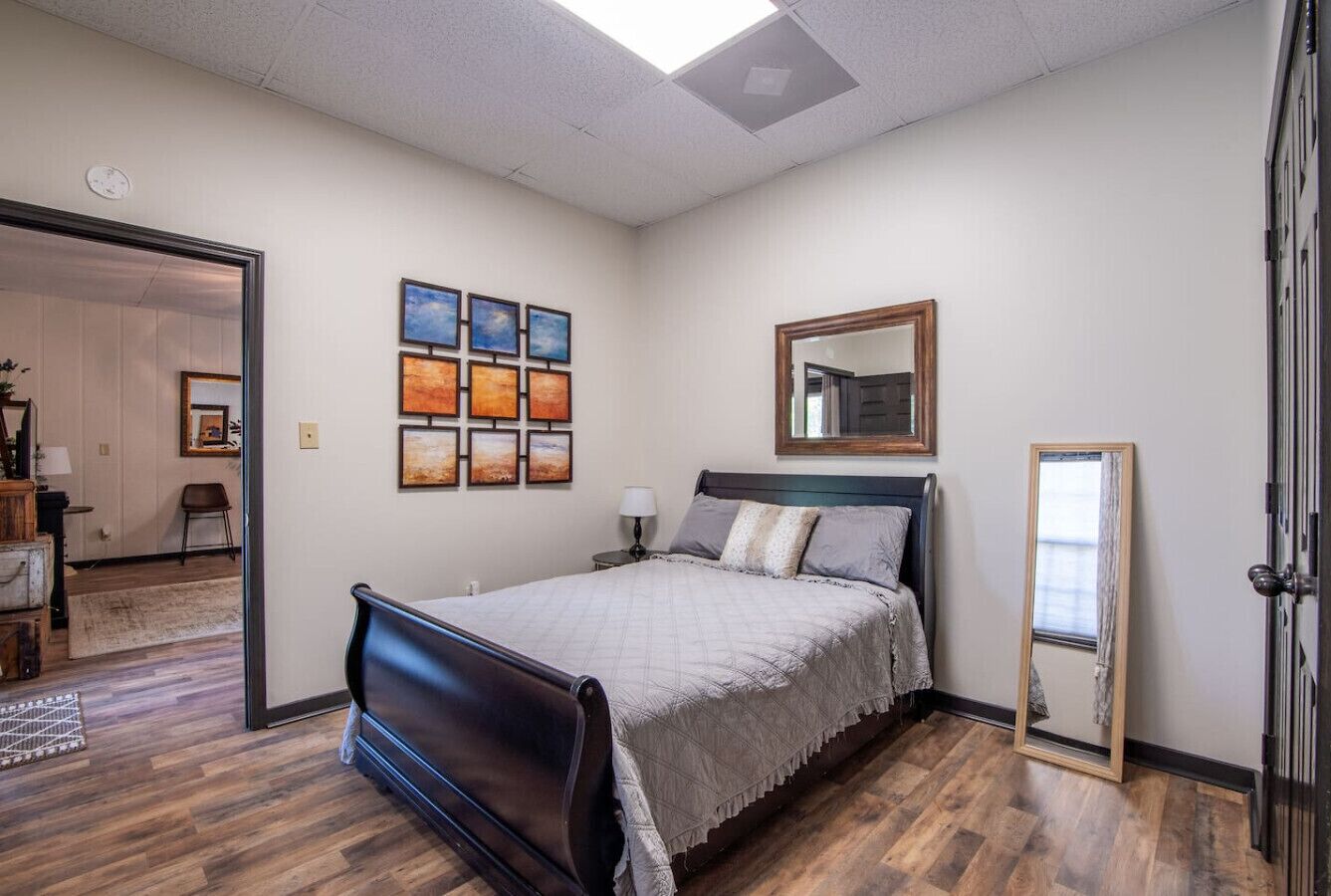 A bedroom with a bed, a nightstand, a mirror, and artwork on the wall.