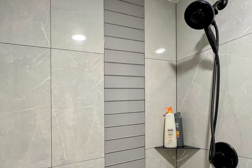 Une salle de bain avec une douche, une étagère contenant des articles de toilette et un mur recouvert de carreaux.