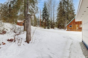 A snowy landscape with a wooden cabin and a modern building with a sloped roof. - Container-home Cottage Near Alyeska & Double Musky (Girdwood)