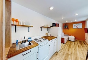 A compact kitchen with a stove, sink, and wooden countertop.