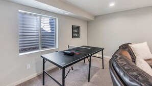 Una habitación con mesa de ping pong, sofá y ventana con persianas.
