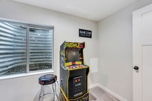 Una habitación con una máquina de juegos recreativos, un letrero que dice 'Game Zone', una ventana con vistas y un letrero que dice 'Give Zone'.