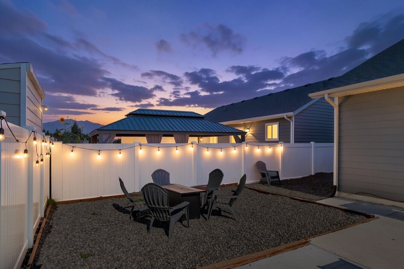 Une terrasse à l’arrière de la maison, avec une table et des chaises, un espace abrité et des guirlandes lumineuses.