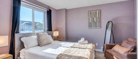 Ein Hotelzimmer mit einem Bett, einem Sessel, einer Lampe, einem Fenster und einem Wandbild.