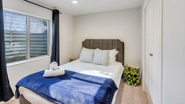 Un dormitorio con cama, ventana, puerta y una mesita de noche.