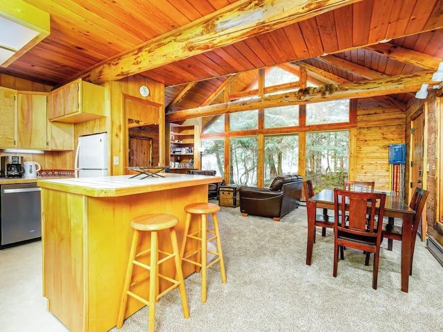 A cabin interior with a kitchen, dining area, and large windows.