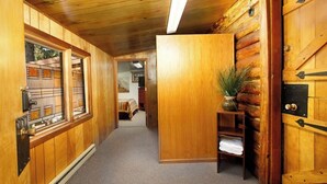 Un couloir intérieur en bois, avec une porte, une fenêtre dotée d’une grille métallique et une plante posée sur une étagère.