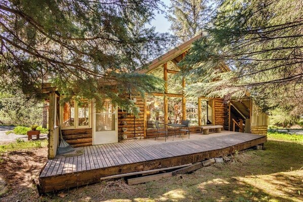 Una cabaña de madera con un balcón, ventanas amplias y una escalera que sube a un nivel superior.