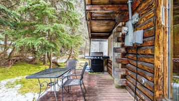 A wooden cabin with a deck, a grill, and a table with chairs.
