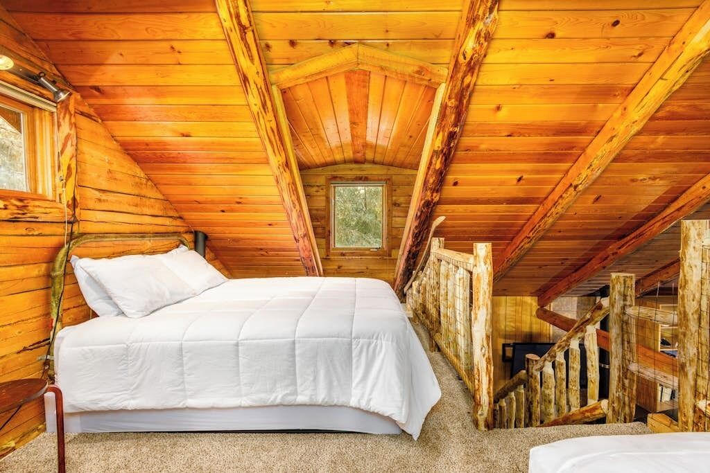 Una habitación de cabaña de madera con una cama, un ventanal y una escalera.