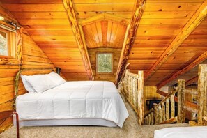Una habitación de cabaña de madera con una cama, un ventanal y una escalera.
