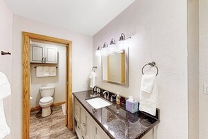 Un baño con lavamanos, espejo, toallero y retrete.