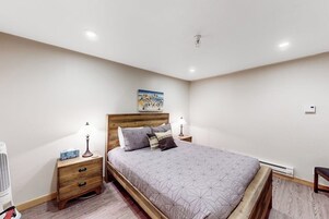 Un dormitorio con cama, cabecero de madera, mesitas de noche y una obra de arte colgada en la pared.