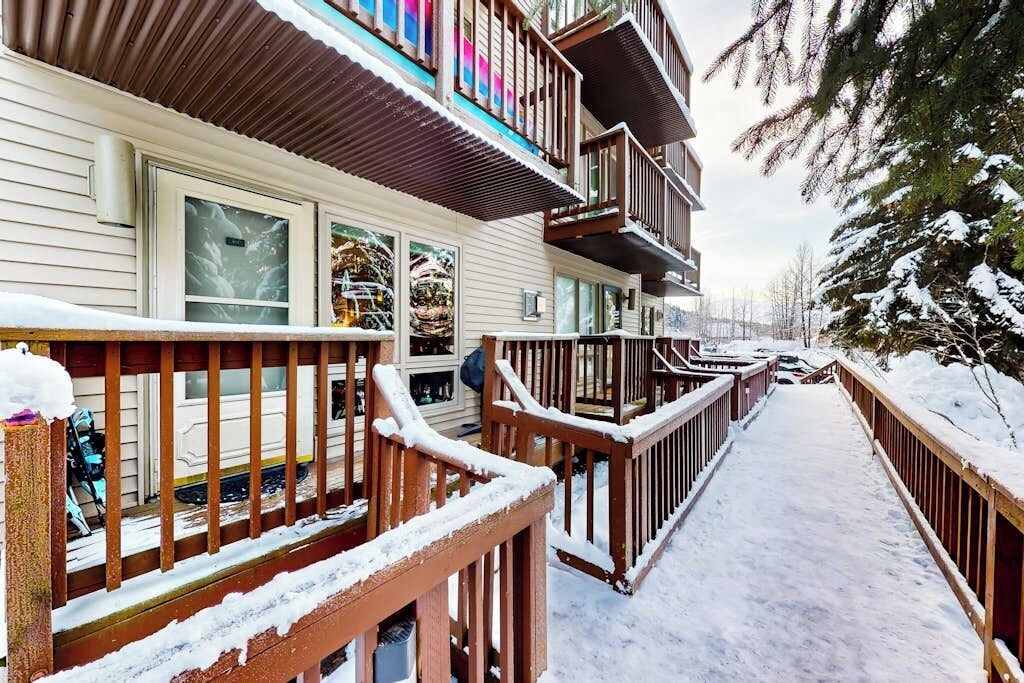 Um edifício de vários andares com um deck e grades de madeira, rodeado por árvores cobertas de neve.
