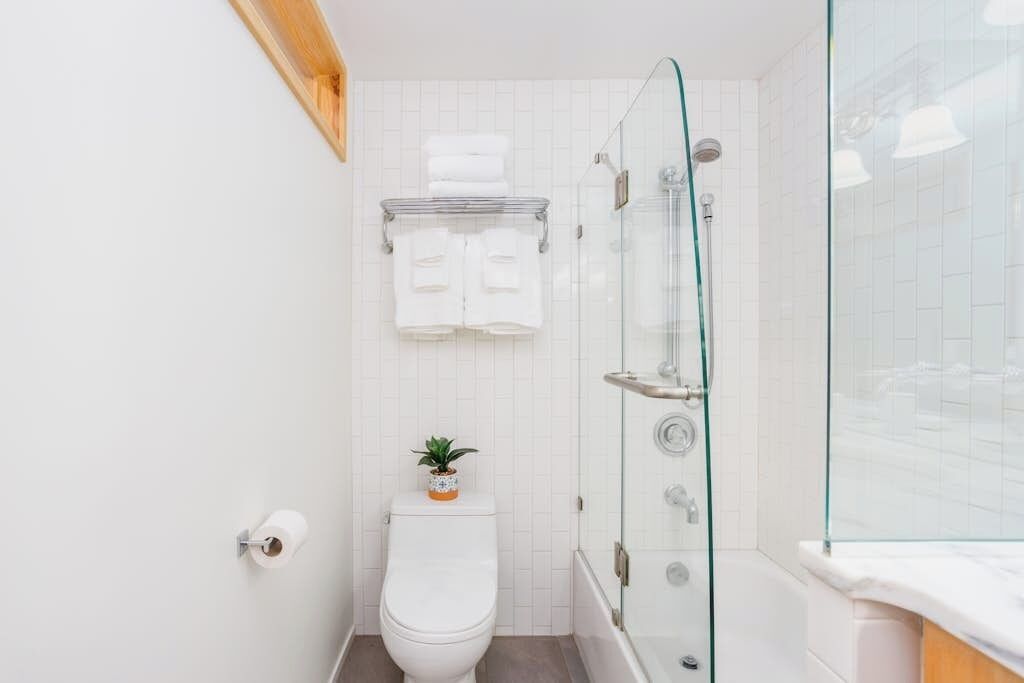 A bathroom with a toilet, a glass shower enclosure, and a towel rack with folded towels.
