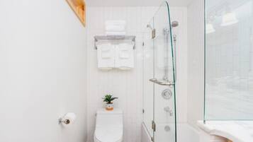 A bathroom with a toilet, a glass shower enclosure, and a towel rack with folded towels.