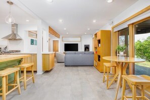 Uma cozinha moderna com uma ilha central, banquetas e um sofá cinzento na área de estar.