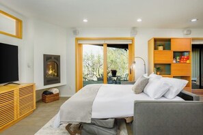 A bedroom with a bed, a television, a fireplace, and a view of the outdoors.