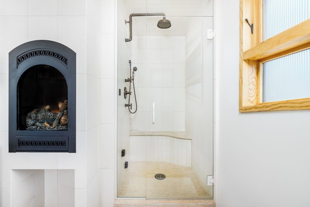 A shower with a glass door, a wooden bench, and a decorative fireplace.
