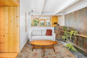 A modern interior with a stone floor, a wooden table, a sofa, and a stone wall with greenery. - Full Downtown Anchorage Triplex for Large Groups (Anchorage)
