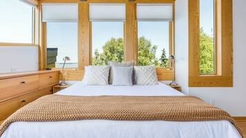 A bedroom with a large bed, wooden headboard, and a view of trees through large windows.
