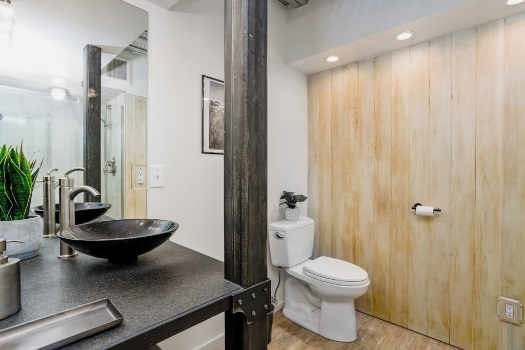 Un baño moderno con un lavabo negro tipo recipiente, un inodoro blanco y una pared de madera.