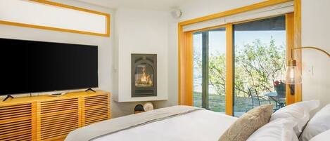 A bedroom with a bed, a television on a wooden console, a fireplace, and a sliding glass door to an outdoor area.