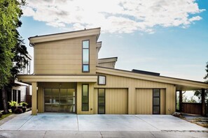 Ein modernes, zweistöckiges Haus mit Garage, großen Fenstern und einer überdachten Terrasse.