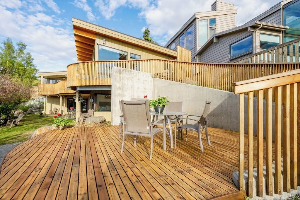 A modern house with a wooden deck, outdoor seating, and a large window overlooking the deck.